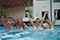 Das Bild ist ein Standbild aus dem Video, das eine fröhliche, im Pool sitzende Familie, die rhythmisch die Arme hochreißen und dabei Wasser hochspritzen.