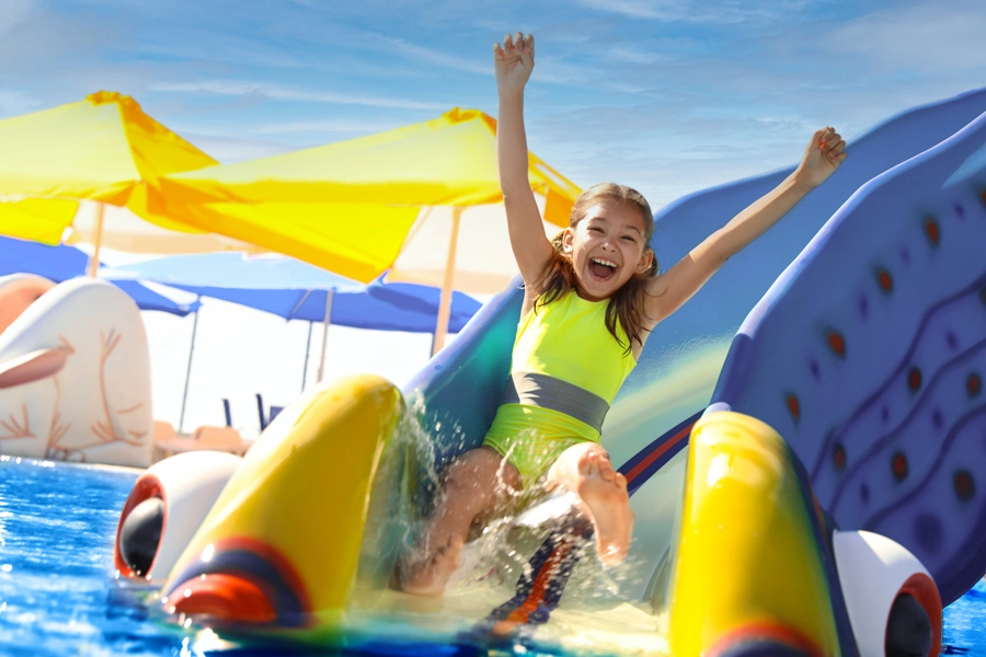 Das Bild zeigt ein Mädchen, das mit in die Luft gerissenen Armen eine Rutsche herunter rutscht und gleich im Schwimmbecken landet.
