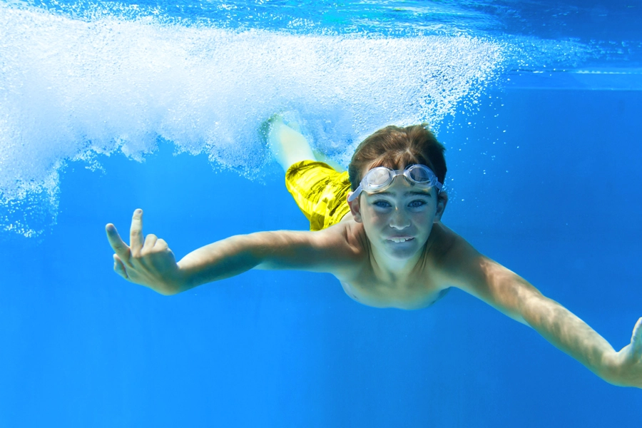 Das Bild zeigt die Unterwasseraufnahme eines tauchenden Jungen, der in die Kamera blickt.
